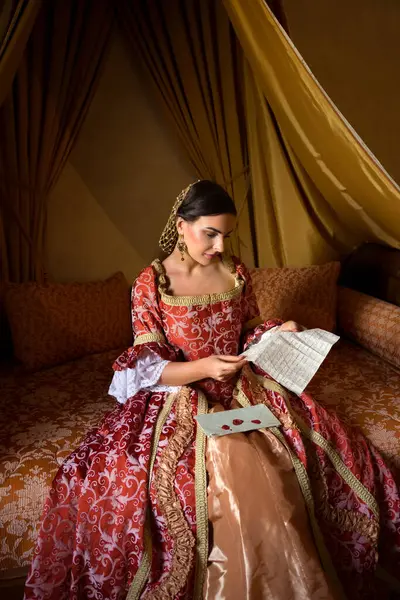 Renaissance lady in late medieval gown sitting on a beautiful canopy bed in her castle bedroom