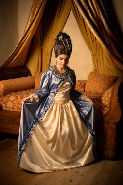 Rokoko kraliçesi Marie Antoinette tarzı giyinmiş ve Fransız şatosunun iç kısımlarında otantik bir peruk takmış güzel bir kadın.