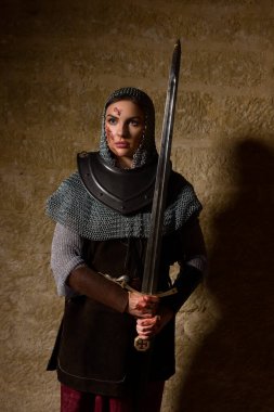 Genç bir kadın ortaçağ şövalyesini canlandırıyor. Deri ceket, zincirli başlık ve metal zırh giyiyor. Joan of Arc tarzı.