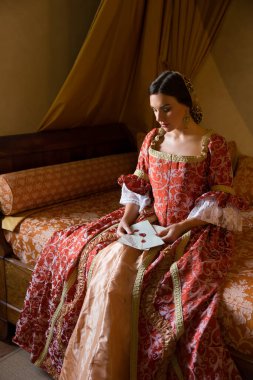 Renaissance lady in late medieval gown sitting on a beautiful canopy bed in her castle bedroom
