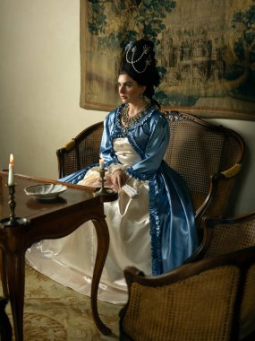 Rokoko kraliçesi Marie Antoinette tarzı giyinmiş ve Fransız şatosunun iç kısımlarında otantik bir peruk takmış güzel bir kadın.