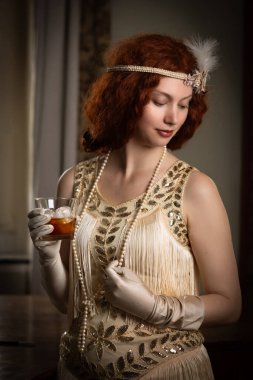 1920 'lerin kızıl saçlı güzel hanımı. Flapper elbisesi. Viskiyle rahatlıyor.