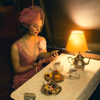 1920 'lerden kalma şık elbiseli bir bayanın otantik bir 1927 model buhar treninin kompartımanında çay içişini canlandırma sahnesi.