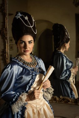 Rokoko kraliçesi Marie Antoinette tarzı giyinmiş ve Fransız şatosunun iç kısımlarında otantik bir peruk takmış güzel bir kadın.