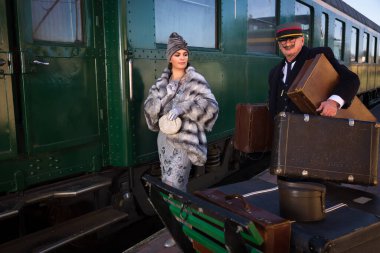 1927 model birinci sınıf bir tren vagonunun yanındaki platformda canlandırma sahnesinde 1920 'lerden kalma lüks bir bayan valizini bekliyor.