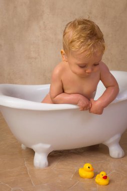 12 aylık küçük tatlı bir çocuğun mutlu sahneleri. Beyaz bir küvette oturmuş, su ve sabunla su sıçratıyor.