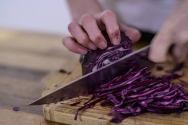 Chopping red cabbage with a kitchen knife on a wooden cutting board