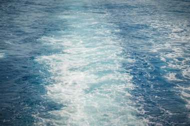 Mavi okyanus yüzeyinde köpüklü, beyaz izler bırakan bir geminin uyanışı.