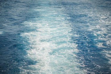 Wake of a ship creating frothy, white trails on the blue ocean surface. clipart