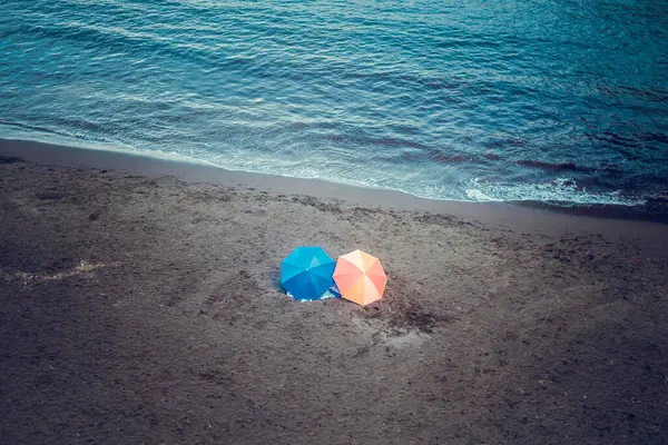 Renkli plaj şemsiyeleri, mavi ve turuncu, arka planda yumuşak deniz dalgaları ve nostaljik atmosferi olan kumlu bir sahilde.