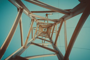 Bir elektrik direğine bakarak, açık mavi gökyüzüne karşı geometrik bir perspektif yaratıyorum.