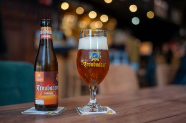 Sint-Niklaas, Belçika, 8 Temmuz 2025, Illustrative Editorial: Bir şişe ve bir bardak Troubadour Magma Belçika Tripel IPA by Brewery The Musketeers in Sint-Gillis-Waas