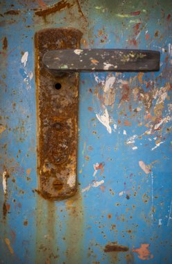 Çok yıpranmış mavi bir yüzeye monte edilmiş paslı metal bir kapı kolunun çok renkli kabuk soyma ve aşınma boyasıyla yakın çekimi..