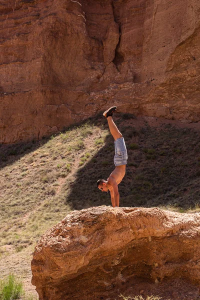 stock image a man of athletic build performing a handstand on a large rock in a canyon gorge, adhering to a healthy lifestyle of proper nutrition