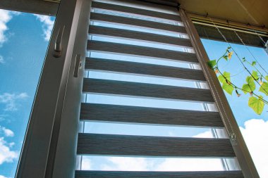 Havalandırmaya açılan plastik bir pencere. Mavi gökyüzüne karşı körlük ve sivrisinek ağı.