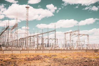 Bozkırda mavi gökyüzüne yakın elektrik santrali ve trafo kuleleri var.