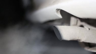 Çalışan bir motoru olan ve duman ve gaz yayan bir otomobil egzoz borusunun görüntüsü gece soğukta, arka plan bulanıklaşır.