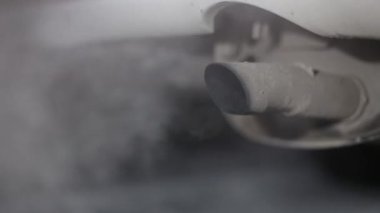 Çalışan bir motoru olan ve duman ve gaz yayan bir otomobil egzoz borusunun görüntüsü gece soğukta, arka plan bulanıklaşır.