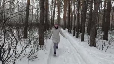 a young girl walks funny in a winter birch forest and shows off, dances and fools around on camera