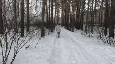 a young girl walks funny in a winter birch forest and shows off, dances and fools around on camera