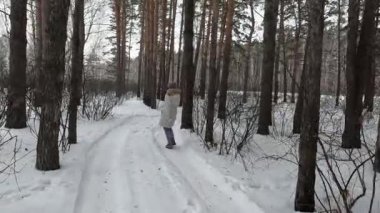 a young girl walks funny in a winter birch forest and shows off, dances and fools around on camera