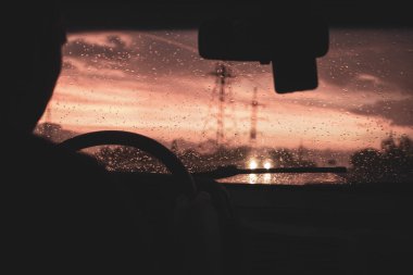 Kötü hava koşullarında, yağmurda ve siste, güzel kırmızı bir günbatımında otoyolda bir arabadan manzara.