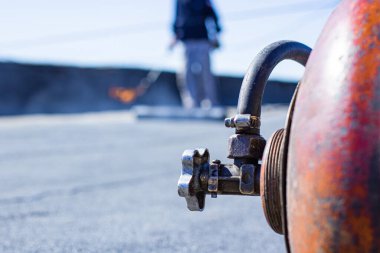 Sıcak bir uygulama yöntemi kullanarak zifte ve asfalta dayalı yumuşak çatı malzemesi kullanan işçiler, ön plan ve arka plan bokeh etkisi ile bulanıklaşır.