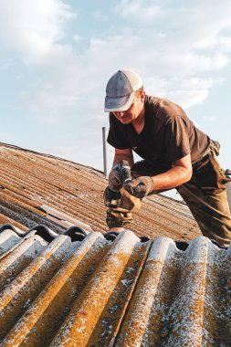 Belediye binasında sigortası olmadan kayrak ve kiremit çatısını tamir eden genç bir adam.