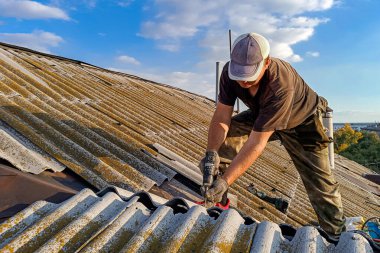 Belediye binasında sigortası olmadan kayrak ve kiremit çatısını tamir eden genç bir adam.