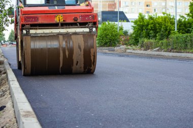 Çalışan insanlar sıcak bir yaz gününde özel ekipmanlarla yeni asfalt döşüyorlar, şehrin sokaklarını düzenliyorlar ve arabalar ve sürücüler için hayatı daha iyi hale getiriyorlar.