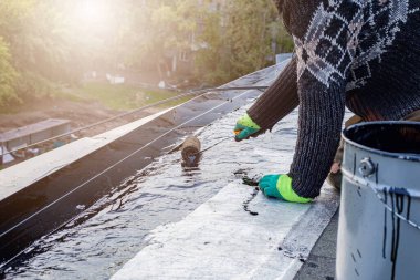 a young worker treats a roof with bitumen primer before applying rolled asphalt roofing using a torch clipart