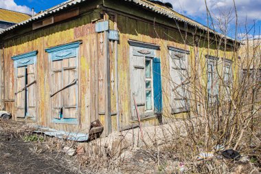 Tahta panjurlu ağaçlar ve çalılarla kaplı eski ahşap parçalanmış özel bir ev.