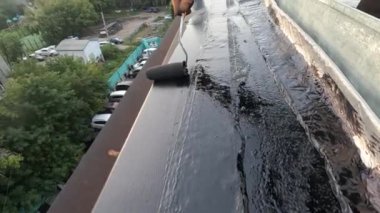 Çatı onarımından önce çatı hazırlayan bir adam, gelecekte bir kentsel gelişimde gün batımının arka planına karşı sızıntıları önlemek için hissetti.