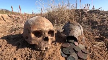 Eski bir yerleşim yerinde metal detektör kullanılarak yapılan bir aramada bulunan bir sürahide bulunan antik madeni para birikintisi ve antik bir şehirdeki bir mezarlıkta bulunan doğal bir kafatası.