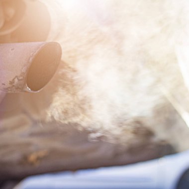 Şehir gelişiminin arka planına yakın çekim yapan araba egzoz borusu, dondurucu bir kış sabahı, parlak güneşin arka planına karşı