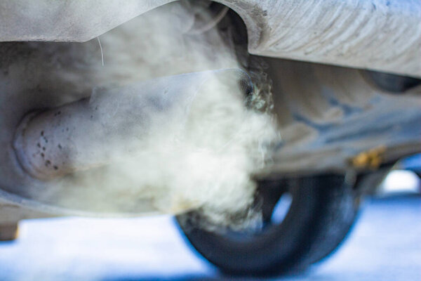 close-up of car exhaust pipe against the backdrop of urban development, on a frosty winter morning against the backdrop of bright sun