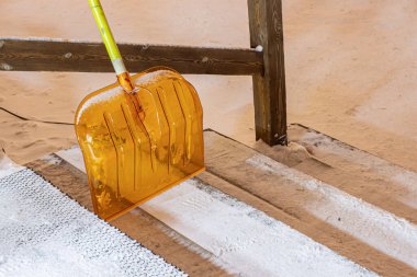 Binanın basamaklarında duran taze kar küreği, turuncu renk, buzlanma sorunu, buzda kayarken insanların yaralanması ve kırılması.