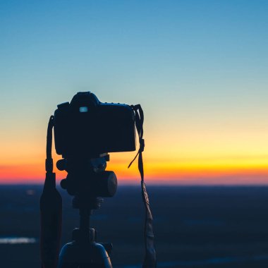 Gün batımında tripodun üzerinde kamera güzel güneşli ufukta uzun pozlu, arka plan bokeh efektiyle bulanık