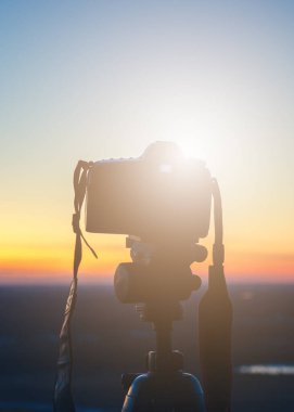 Gün batımında tripodun üzerinde kamera güzel güneşli ufukta uzun pozlu, arka plan bokeh efektiyle bulanık