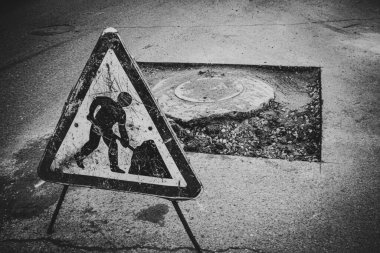 a close-up of a road repair sign against the backdrop of a broken highway with potholes and bumps in need of repair clipart