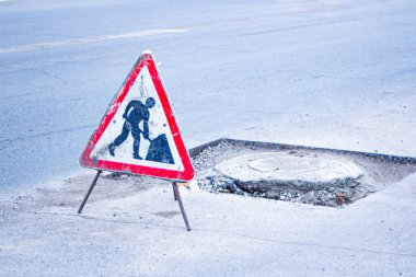 a close-up of a road repair sign against the backdrop of a broken highway with potholes and bumps in need of repair clipart