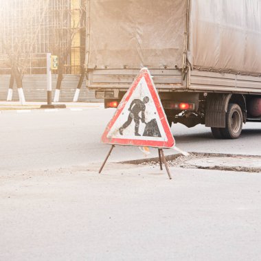 Bozuk bir otoyolun arka planında yol tabelasına yakın çekim. Çukur ve tümseklerin onarılması gerekiyor.