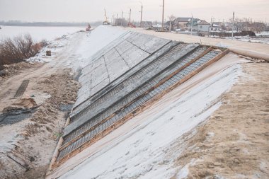 Kaynak sellerine ve eriyen sulara karşı korunmak için rulo malzemeler ve beton kullanarak koruyucu bir baraj inşa etmek