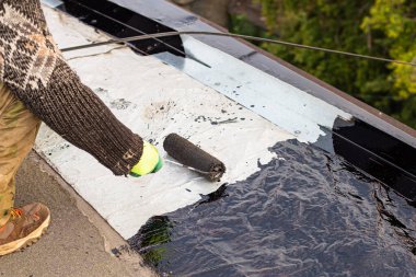 Genç bir işçi, meşale kullanarak asfalt çatı kaplamasını kullanmadan önce çatıyı bitumen astar ile kaplıyor.