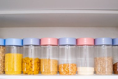 Mutfakta çeşitli tahıl ve tohumlarla raflar - bezelyeler, ayçiçeği ve balkabağı tohumları, fasulyeler, pirinç, makarna, yulaf ezmesi, kuskus, mercimek, cam kavanozlarda bulgur 