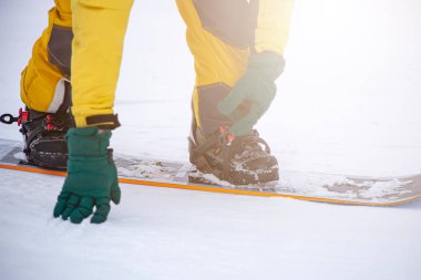 Kayak merkezindeki yüksek dağdaki snowboardcu gün batımında bağlayıcı ve yakın plan kayışlara bağlanıyor.