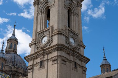 Bazilika del Pilar 'ın saat kulesine yakın çekim, tarihsel ve işlevsel mimarinin sakin bir gökyüzüne karşı birleşimi.