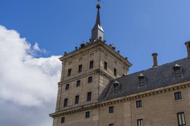 Heykel detayları ve El Escorial Manastırı 'nın ikonik kubbesi kabarık bulutlu mavi gökyüzüne karşı duruyor.