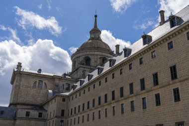 Heykel detayları ve El Escorial Manastırı 'nın ikonik kubbesi kabarık bulutlu mavi gökyüzüne karşı duruyor.