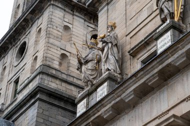 İncil krallarının yaldızlı heykelleri, El Escorial Manastırı cephesini süslüyor, taş duvarlara dayanıyor ve yazılı plaketler çiziliyor..